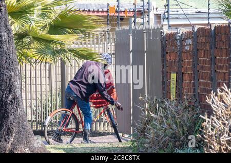 Alberton, Afrique du Sud - un postier non identifié livre le courrier à vélo aux maisons dans une image de quartier résidentiel en format horizontal Banque D'Images