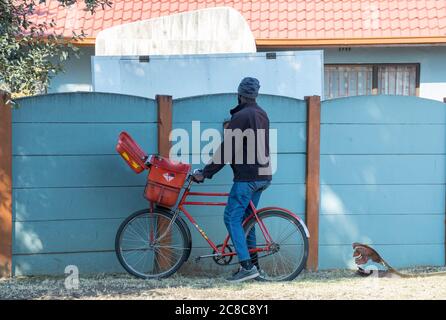 Alberton, Afrique du Sud - un postier non identifié livre le courrier à vélo aux maisons dans une image de quartier résidentiel en format horizontal Banque D'Images
