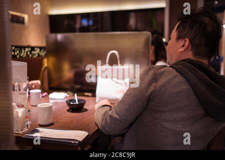 Hsinchu / Taiwan - 15 juillet 2020: Homme mangeant dans la table de restaurant divisée par des murs en plastique pour maintenir la distance sociale pendant la pandémie du coronavirus Banque D'Images