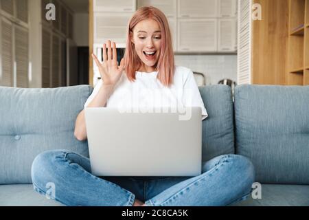 Image d'une femme excitée qui utilise un ordinateur portable et se fait main tout en étant assise sur un canapé à la maison Banque D'Images