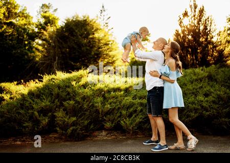 Famille heureuse et aimante faites du plaisir avec un bébé mignon, un père fort ascenseur dans l'air souriant fille, les parents jouent avec l'enfant au parc Banque D'Images