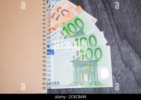 Ordinateur portable et de l'argent sur la table. Le bloc-notes et billets sur fond de bois sombre. La planification d'affaires et de voyage concept. Banque D'Images