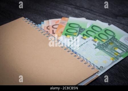 Ordinateur portable et de l'argent sur la table. Le bloc-notes et billets sur fond de bois sombre. La planification d'affaires et de voyage concept. Banque D'Images