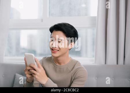 Homme heureux de regarder du contenu multimédia dans un téléphone intelligent assis sur un canapé à la maison Banque D'Images