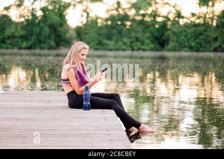 athlète utilisant un smartphone après l'entraînement - femme de forme caucasienne dans les vêtements de sport en utilisant un téléphone portable Banque D'Images