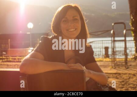 Une femme caucasienne sourit en regardant la caméra au coucher du soleil, derrière elle. Concept de paix et de sérénité. Banque D'Images