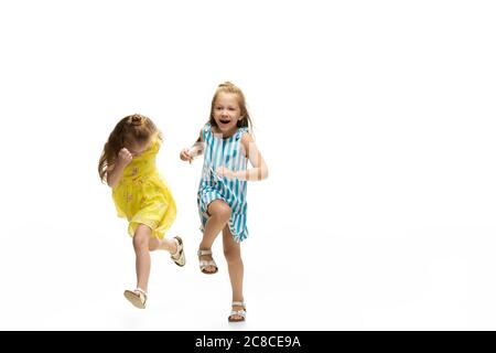 Enfants heureux, petites et émotionnelles filles caucasiennes sautant et courant isolées sur fond blanc. Il a l'air heureux, gai, sincère. CopySpace pour publicité. Enfance, éducation, concept de bonheur. Banque D'Images