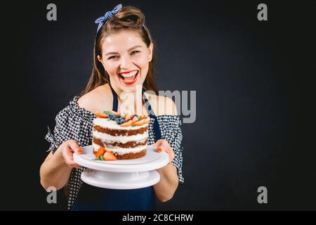 Bonne charmante petite femme de style épinglette, souriante, avec un gâteau au chocolat Banque D'Images