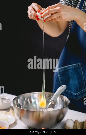 Vue rognée de la femme qui casse les mains de l'œuf pour la pâte à gâteau Banque D'Images