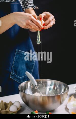Vue rognée des mains de la femme cassant l'œuf dans un plat en acier Banque D'Images