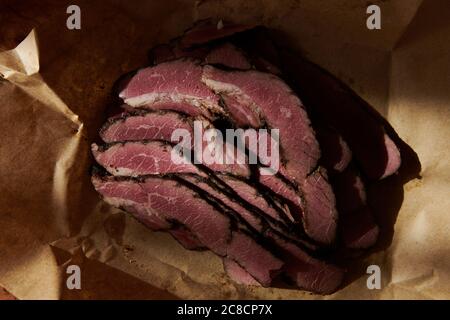 Appétissant pastrami sur un papier kraft. Tranches de viande de bœuf cornées par lumière du coucher du soleil. Viande biologique de fermier. Plat traditionnel juif. Banque D'Images