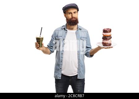 Homme barbu tenant un smoothie vert et une assiette de beignets au chocolat, nourriture saine contre malsaine, isolé sur fond blanc Banque D'Images