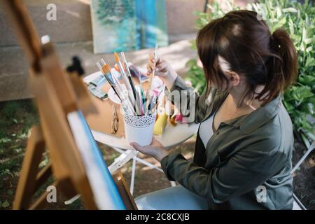 Brunette femme tenant pot avec pinceaux à l'extérieur Banque D'Images