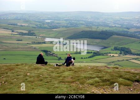 Un couple assis et appréciant la vue avec des chiens de réservoirs de mousse noire du sommet de Pendle Hill, Barley, Lancashire, Royaume-Uni. Banque D'Images