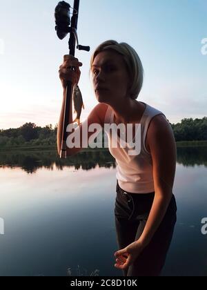 Jeune femme pêche sur la rivière au coucher du soleil Banque D'Images