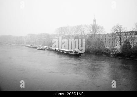 Des Péniche en chute de neige sur la Marne qui traverse les banlieues parisiennes. Banques inondées. Crépuscule brumeux le soir. Mouvement flou des flocons de neige. Noir blanc Banque D'Images