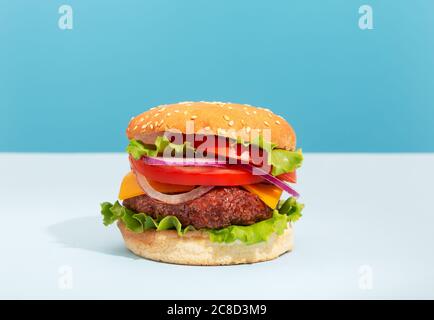 Hamburger de bœuf frais et juteux avec frites placées sur du bleu arrière-plan créatif et tendance Banque D'Images