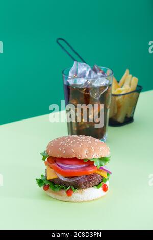 Hamburger de bœuf frais juteux placé sur fond vert créatif avec pommes de terre et boisson, orientation verticale isométrique Banque D'Images