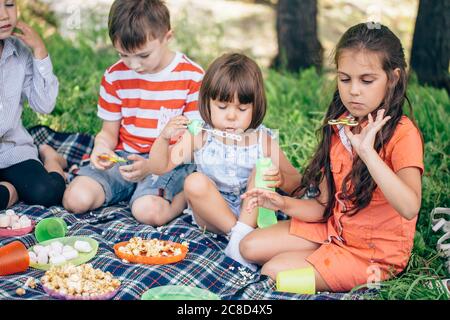 Une petite fille mignonne et ses sœurs plus âgées soufflent sur un disque coloré dans le jardin. Banque D'Images