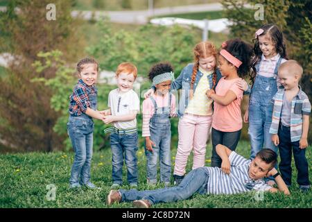 Enfants, garçons et filles jouant, plaisantant, se blotchant et s'amusant au coucher du soleil dans le parc sur l'herbe verte Banque D'Images