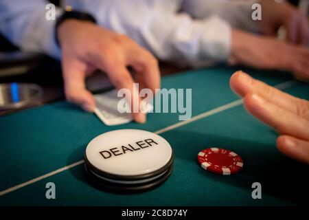 Gros plan photo de la main d'un donneur et badge sur une table de casino avec les mains des joueurs en arrière-plan Banque D'Images