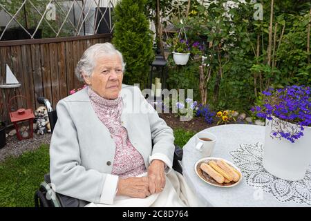 Une vieille femme en fauteuil roulant buvant du thé sur la terrasse. Photo de haute qualité Banque D'Images