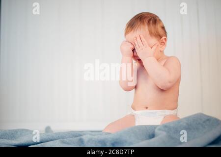 un petit bébé pleure sur le lit au-dessus du mur blanc Banque D'Images