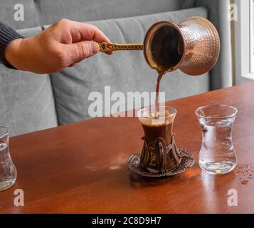 Une main de barista de sexe masculin verse du café turc frais d'un turc dans un magnifique verre de style oriental. Banque D'Images