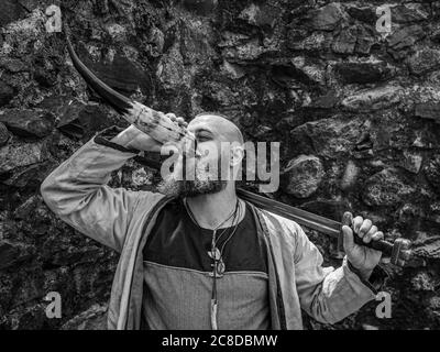 Guerrier viking avec une barbe épaisse et de grandes boissons d'épée de la corne devant un mur de pierre, image historique noir et blanc repici Banque D'Images