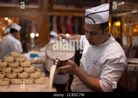 Damas, Syrie 03/28/2010: Un chef portant une robe blanche et un chapeau verse de la crème fraîche dans des tasses en verre à partir d'un pichet en métal. Cet endroit (Bakda Banque D'Images