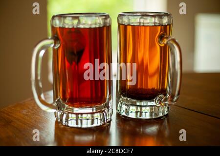 Image de près de deux grandes tasses à bière en verre remplies de thé noir frais. Les mugs sont assis sur un seuil de fenêtre ouvert avec des arbres en arrière-plan. Banque D'Images