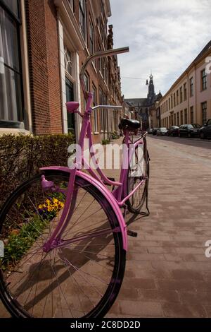 Vue rapprochée d'un vélo d'époque peint en aérosol rose, stationné dans un quartier résidentiel d'Amsterdam. Le vélo est opérationnel avec une dynamo et un flash Banque D'Images