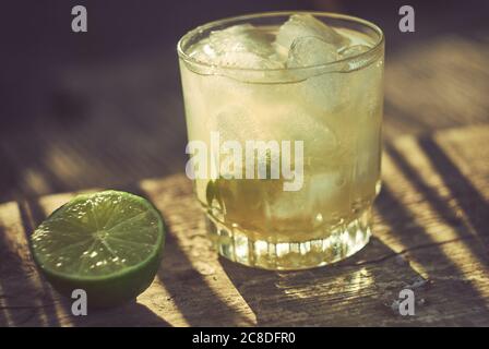 Un cocktail Caipirinha avec un coin de lime sur le côté, tourné à l'extérieur dans les longues ombres de la lumière du soir. Banque D'Images