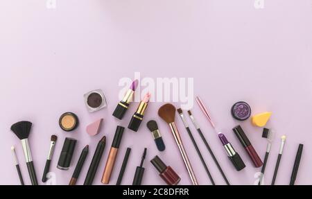 Maquillage cosmétiques plat. Rouges à lèvres et vernis à ongles, ombres à paupières et mascara, pinceaux et crayons sur fond de couleur violet pastel, espace de copie Banque D'Images