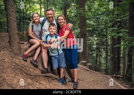 Portrait de parents souriants et de leurs deux petits enfants debout ensemble sur un chemin dans une forêt pendant une randonnée Banque D'Images