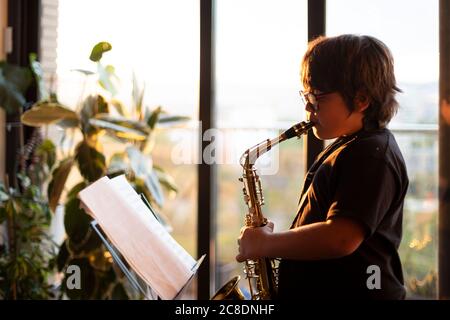 Garçon s'exerçant pour jouer le saxophone à la maison dans le soirée Banque D'Images