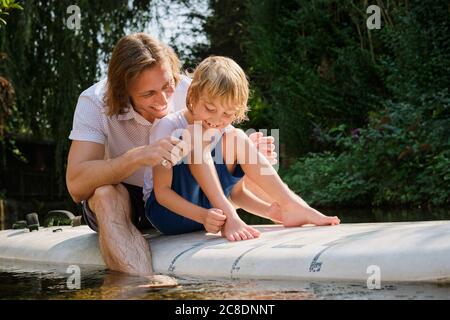 Un père et un fils heureux assis sur un paddleboard dans le ruisseau à forêt Banque D'Images