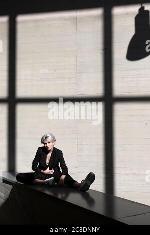 Femme d'affaires élégante portant un costume élégant se détendant sur le mur de maintien avec lumière du soleil et ombre en arrière-plan Banque D'Images