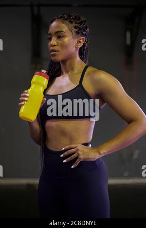 Une athlète féminine attentionnée tenant une bouteille d'eau tout en se tenant à la salle de gym Banque D'Images