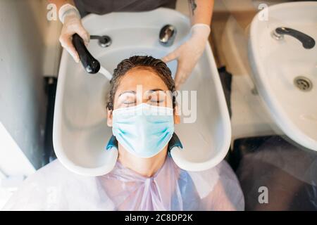 Femme avec masque se laver les cheveux dans un salon de coiffure Banque D'Images