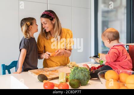 Une mère et une fille souriantes préparent la nourriture pendant que leur fille joue sur l'île de cuisine Banque D'Images