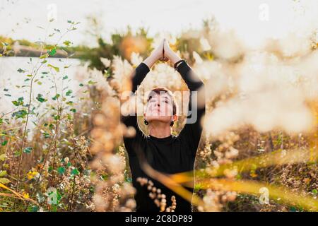 Femme avec les yeux fermés et les bras levés s'exerçant en position debout parmi les plantes Banque D'Images