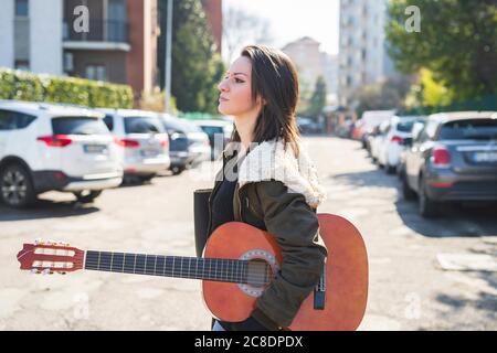 Femme adulte de taille moyenne transportant de la guitare tout en marchant sur la route ville Banque D'Images