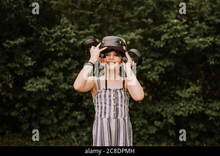 Fille souriante portant un simulateur de réalité virtuelle debout contre les plantes cour Banque D'Images