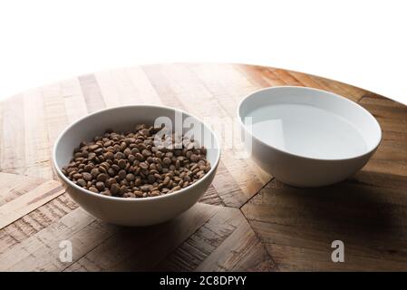 plats pour chats - deux bols blancs d'aliments secs pour chats et d'eau sur une table en bois devant un fond blanc Banque D'Images