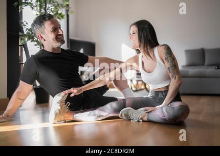 Couple souriant parlant tout en faisant de l'exercice sur le parquet à la maison Banque D'Images