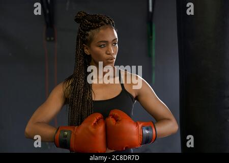 Jeune femme aux cheveux tressés portant des gants de boxe rouges salle de sport Banque D'Images