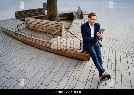 Homme d'affaires souriant assis sur un banc en bois à l'aide d'une tablette Banque D'Images