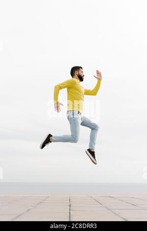 Un jeune homme insouciant sautant sur le sentier contre un mur blanc Banque D'Images