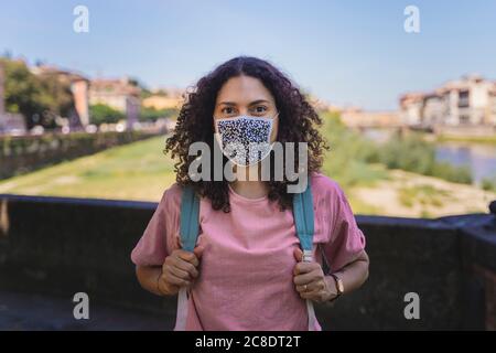 Femme portant un masque de protection debout avec sac à dos en ville contre le ciel Banque D'Images